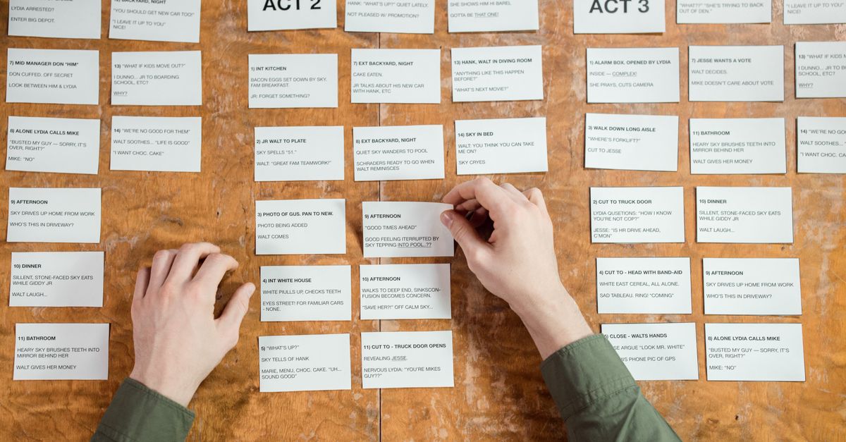 Hands arranging screenplay cards on a wooden table, depicting script development.